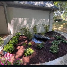 Completed backyard garden with brick pathway, mulch, shrubs, and fountain feature