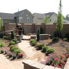 Backyard landscape installation with new plants, brick walkway, and raised seating area
