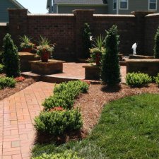Brick pathway garden design with shrubs, flowers, and raised seating area