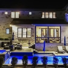 Illuminated backyard pool and patio area with modern landscape lighting