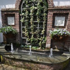 Backyard landscape design with raised brick patio, decorative fountain, and garden beds