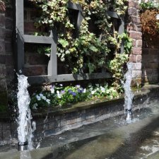Close-up of brick garden fountain with cascading water and ivy trellis