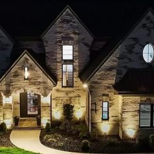 Warm architectural uplighting on a large stone home at night