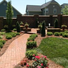 Finished backyard landscape with brick walkway, shrubs, and mulched beds