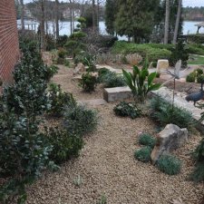 Gravel garden beds with shrubs and stone accents near brick wall