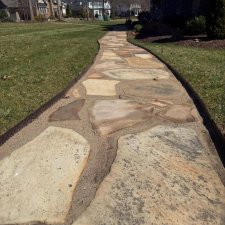 Close-up of curved flagstone walkway set in sand along residential lawn