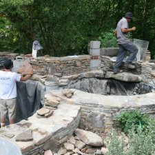 Workers building a custom stone pond with waterfall features