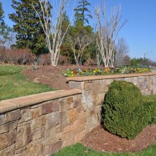 Stacked stone retaining wall with raised landscape bed along roadside