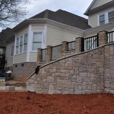 Large stone retaining wall with upper-level railing near residential home