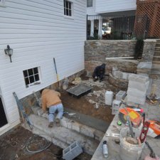 Retaining wall construction with workers installing stone steps and block foundation