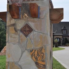 Stone entry column with decorative inlay and timber accents at residential driveway