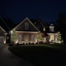 Brick home decorated with holiday lights on trees and shrubs