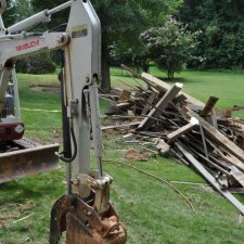 Construction debris pile beside mini-excavator during landscape teardown