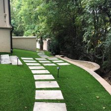 Side yard walkway with evenly spaced rectangular pavers set into artificial turf