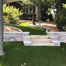 Artificial turf walkway with stone steps in landscaped backyard