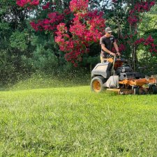 Lawn care technician mowing tall grass near flowering trees