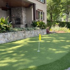 Backyard putting green installation beside stone patio