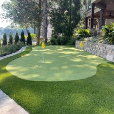 Backyard putting green surrounded by stone and landscape plants