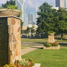 Urban landscape design featuring stone pillars with planters and flower beds in front of city skyline