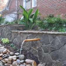 Stone wall water feature with multiple spouts flowing over river rock